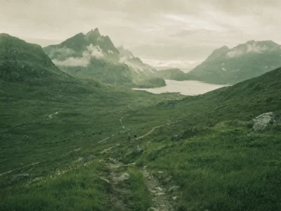 Footpath winding through a green valley toward misty fjord peaks on an adventure trip