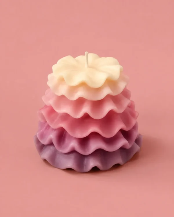 Sculptural ruffle-tiered candle shading from cream to lilac on a pink studio background