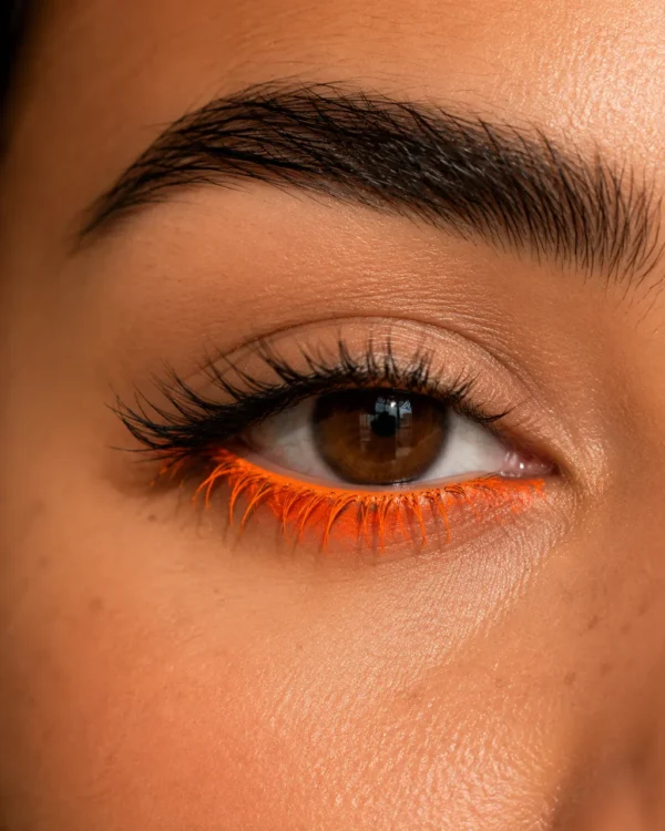 Macro beauty close-up of an eye with bright orange eyeliner and a full brow
