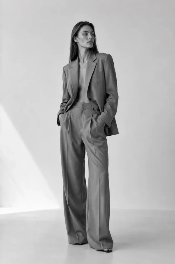 Slim model in a taupe wide-leg suit standing in soft studio light, full-length editorial fashion portrait