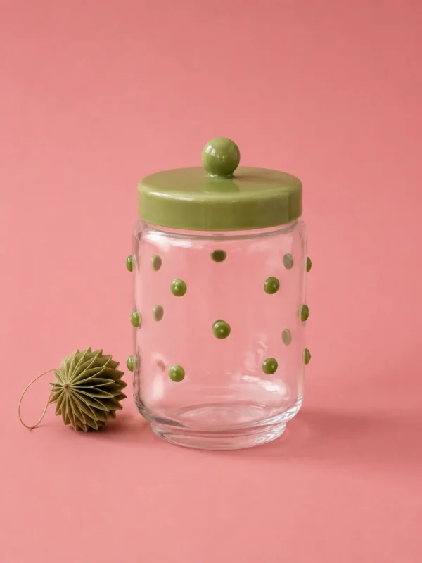 Clear glass storage jar with green polka dots and a green lid on a pink background