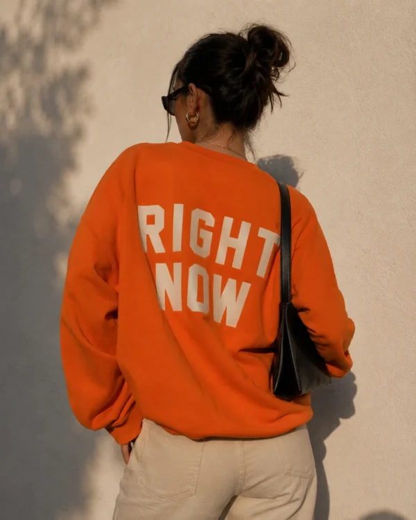 Influencer photographed from behind in an orange Right Now sweatshirt in hard sunlight