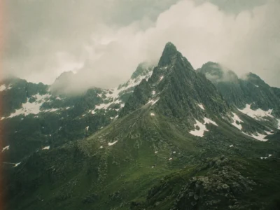 Jagged mountain peak wreathed in low cloud with patches of snow on an adventure trip