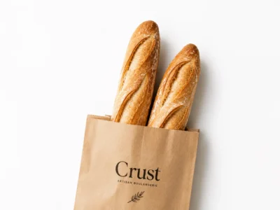 Two crusty baguettes in a kraft paper bag printed with the Crust artisan boulangerie logo