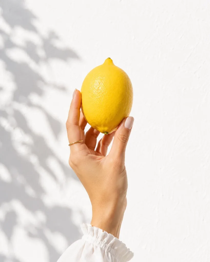 Hand holding a single lemon against a white wall with leaf shadows
