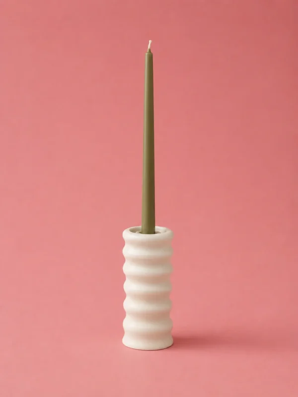 Sage green taper candle standing in a short white ribbed ceramic holder on pink