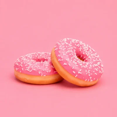Two pink-glazed donuts with sprinkles stacked on a flat pink studio background