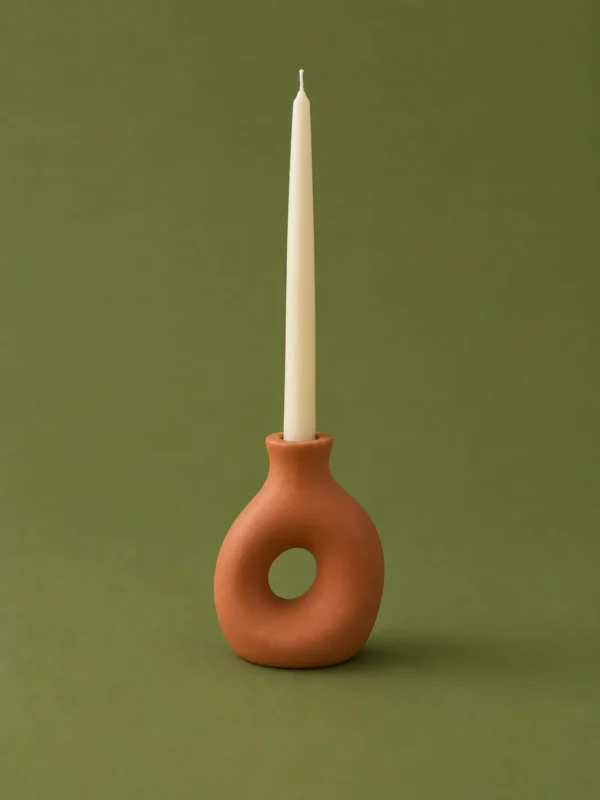 Cream taper candle in a terracotta doughnut-shaped holder on an olive background