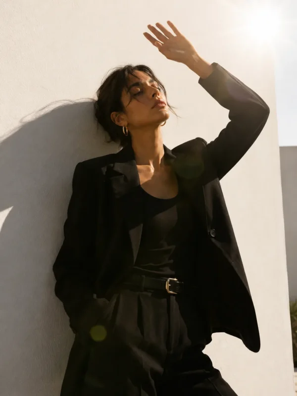 Influencer in a black leather jacket posing with a raised arm against a sunlit wall