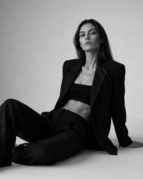 Model in an open blazer and bralette seated on the studio floor with legs extended, editorial fashion portrait