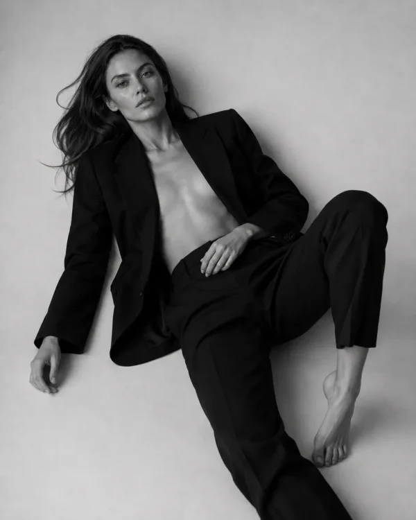Model in an open black suit seated on the floor leaning against a wall, relaxed editorial fashion portrait