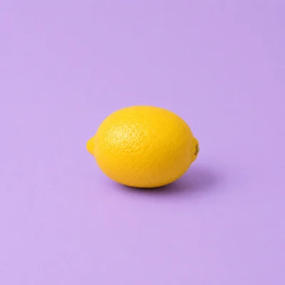 Single whole lemon resting on a flat lavender studio background