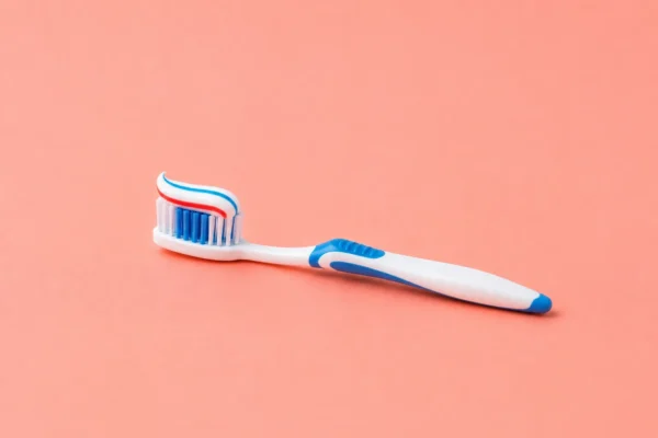Blue and white toothbrush laid flat on a warm coral studio background