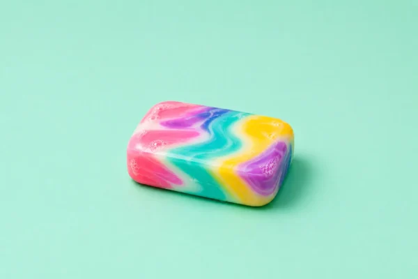 Tie-dye swirled bar of soap resting on a flat mint-green background